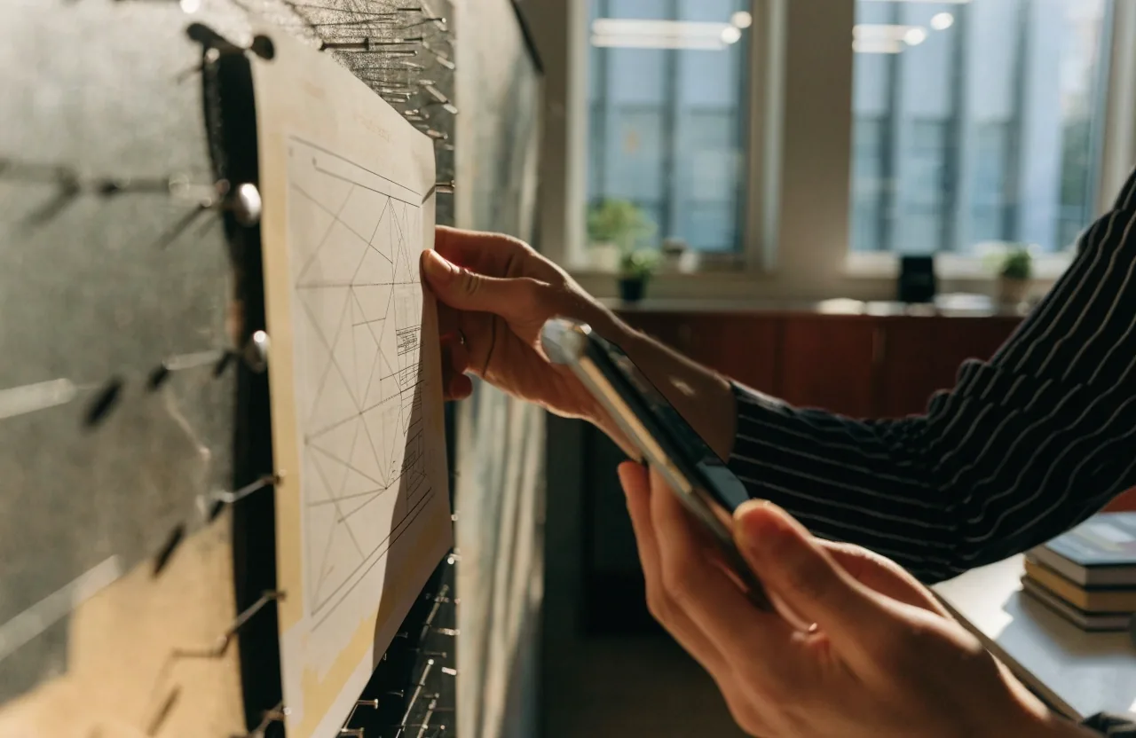 A marketing team's workspace with a printed layout pinned to a board and a phone on the desk